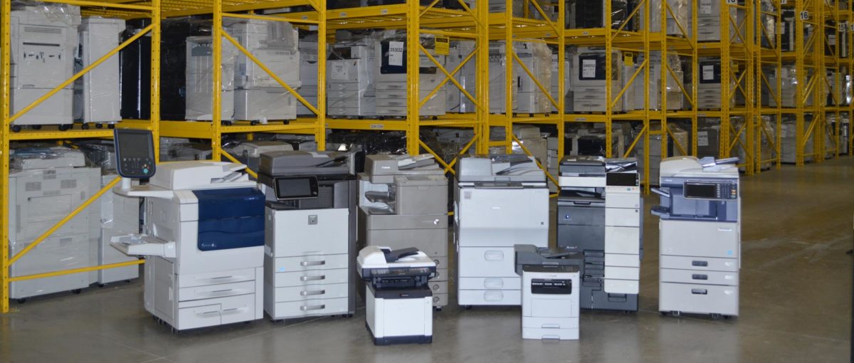 6 large and 2 small copiers ranged in front of warehouse shelves of copiers